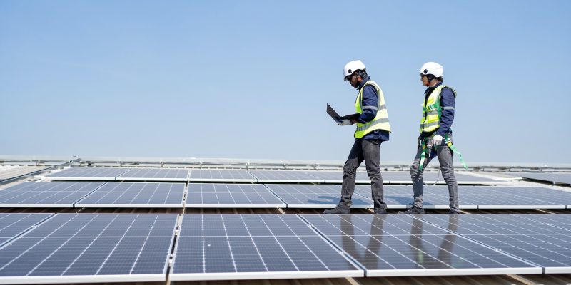 engineer-on-rooftop-stand-next-to-solar-panels-discussion-with-team-check-laptop-for-installation.jpg